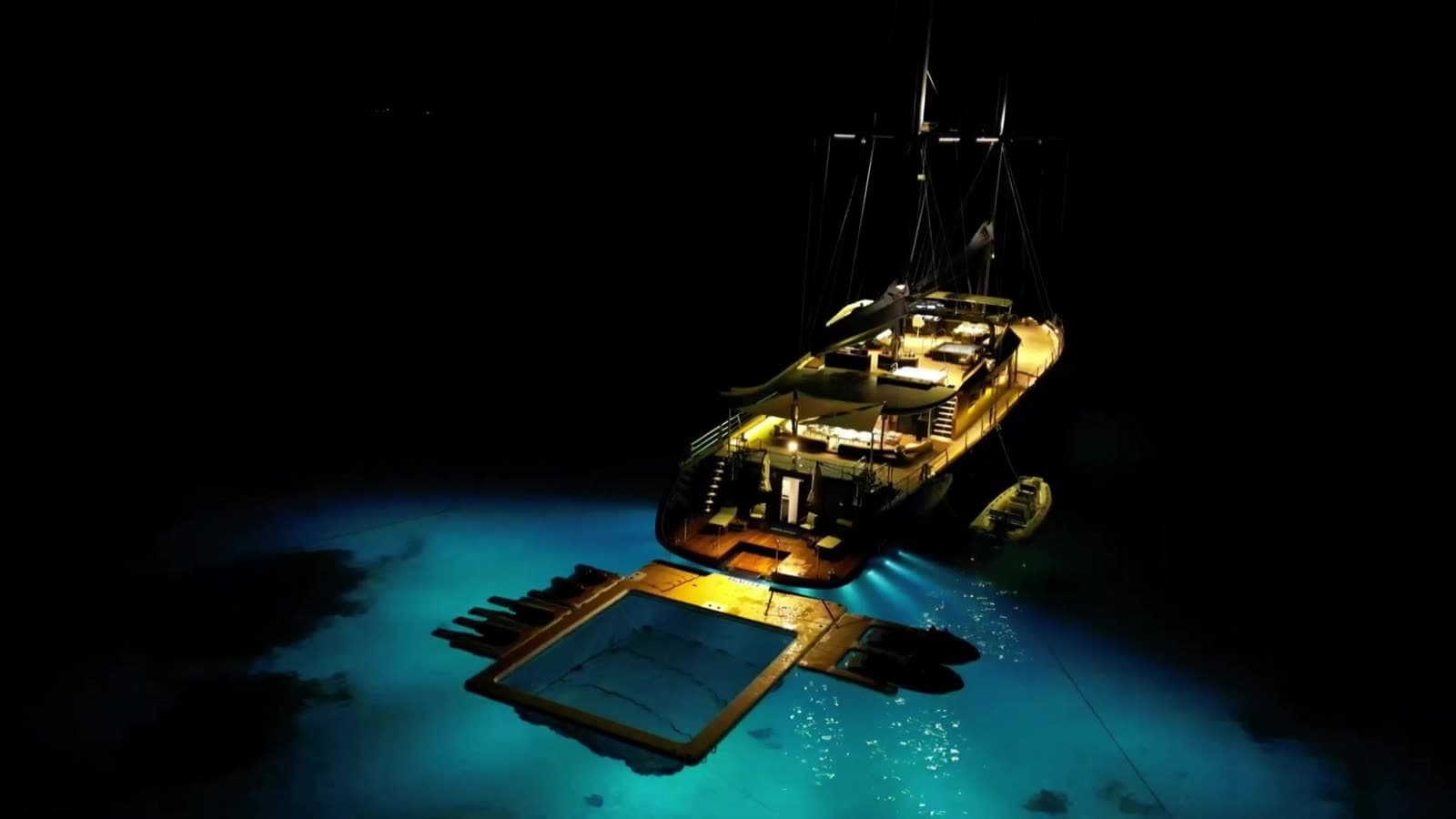 A private sailing yacht at anchor after dark, its golden-lit decks above turquoise water