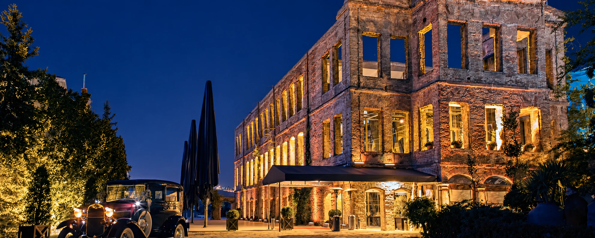 A historic brick mansion lit for an evening event, with a vintage car waiting outside