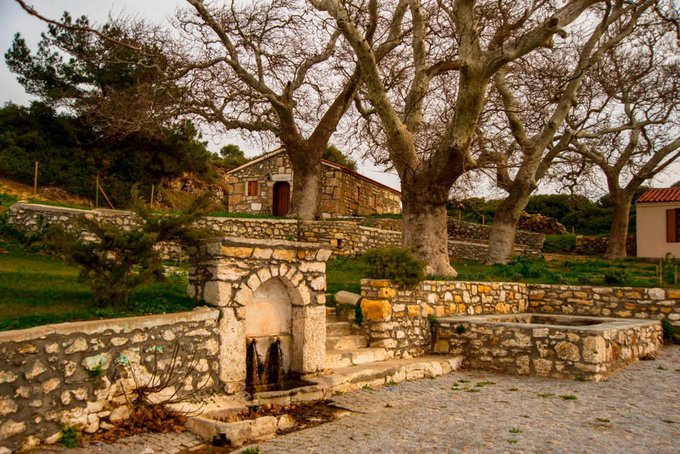 The stone courtyard and fountain of Agia Paraskevi shaded by old plane trees