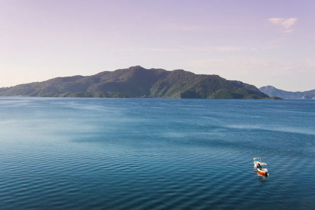 A small boat on calm blue water beneath a forested island