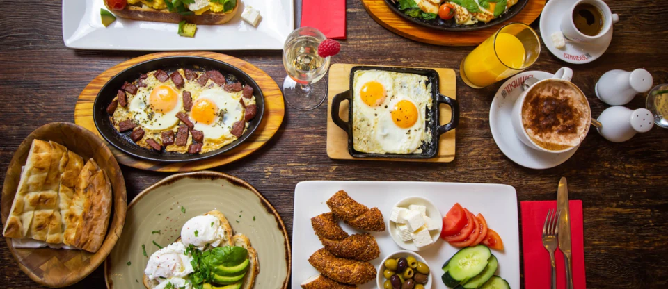 A generous kahvalti spread of eggs, olives, cheeses, simit, and fresh vegetables on a wooden table.