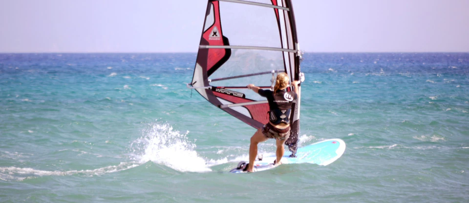 A windsurfer carving across turquoise Aegean water.