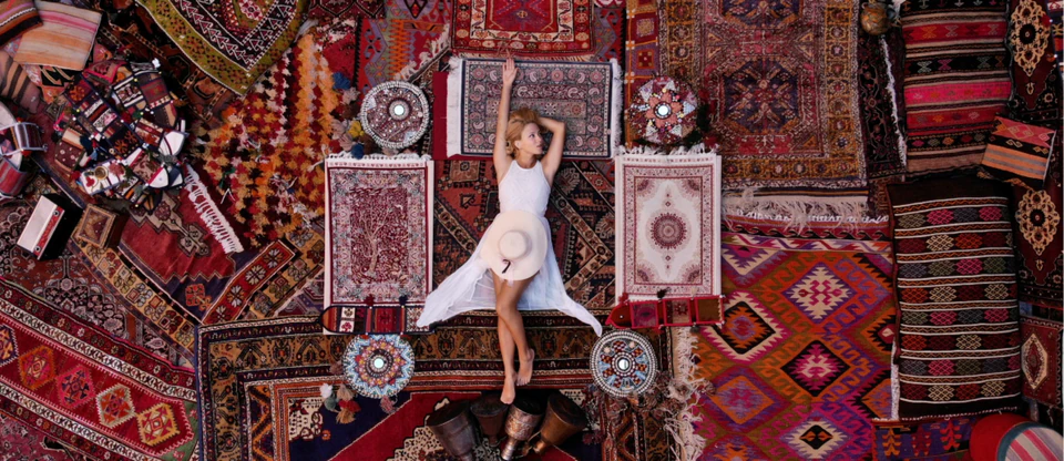 A traveller surrounded by richly patterned Turkish carpets and kilims