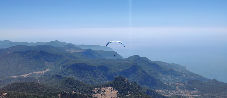 A paraglider soaring high above forested mountains and the sea near Oludeniz.