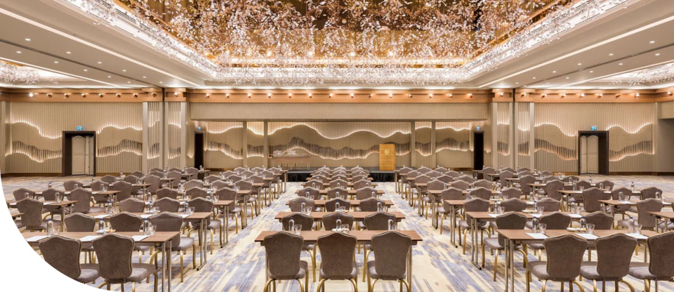 A grand ballroom set for a conference beneath a canopy of crystal lights