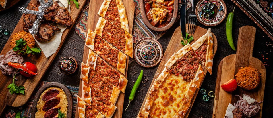 Boat-shaped pide, kebabs, and mezes arranged on wooden serving boards.