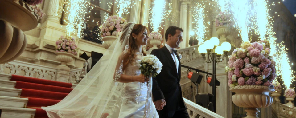 A bride and groom descend a grand staircase amid flowers and cascading sparklers