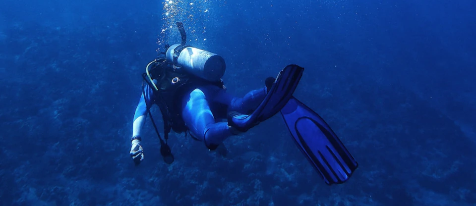 A scuba diver finning through deep blue water, trailed by rising bubbles.