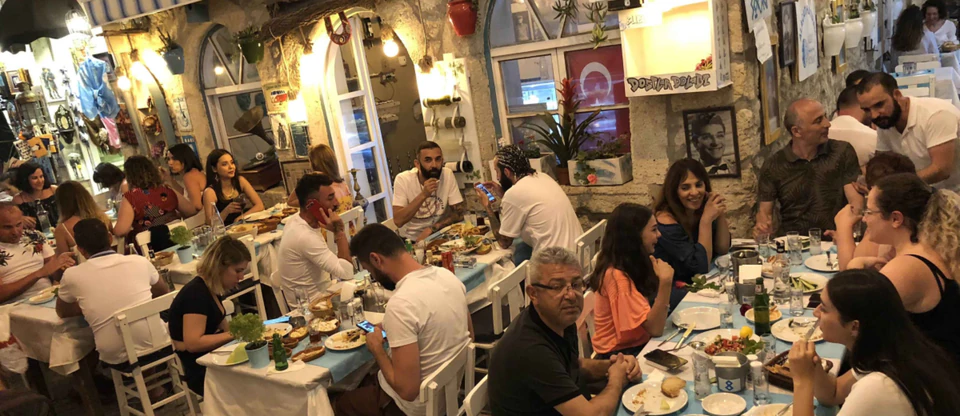 Friends sharing meze in a lively stone-walled traditional taverna (meyhane).
