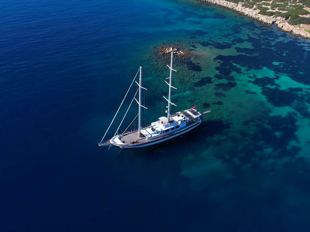 A two-masted wooden gulet at anchor in a turquoise cove, seen from above