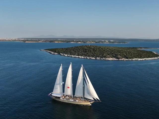 A large three-masted gulet under full sail off a green island