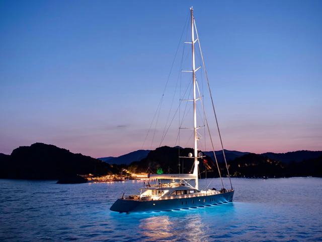 An illuminated single-masted sailing yacht at anchor at dusk
